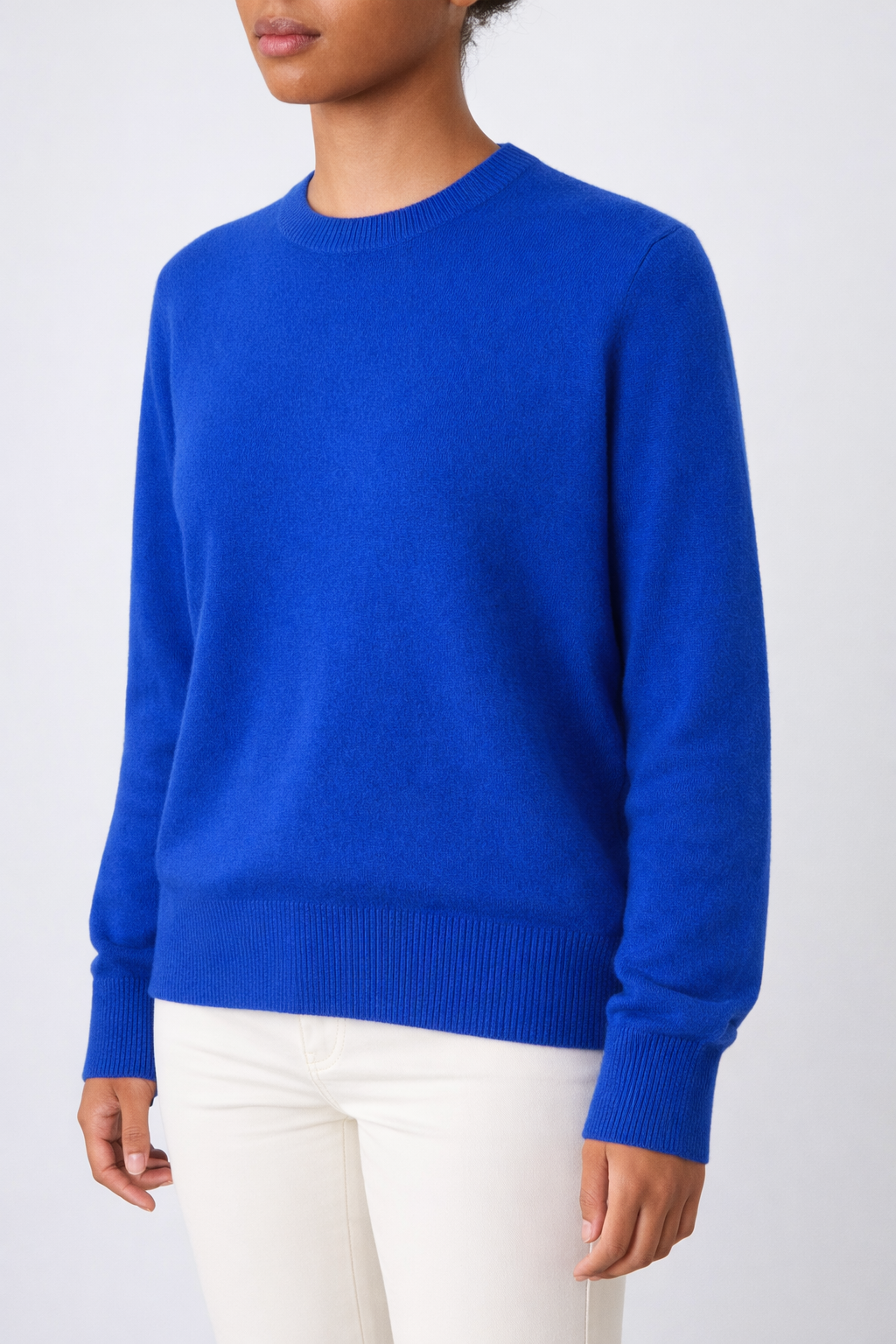 A person wearing the We Norwegians Blefjell Crewneck Women - Pure Cashmere in bright blue and off-white pants stands against a plain light background, with their head partially out of the frame.