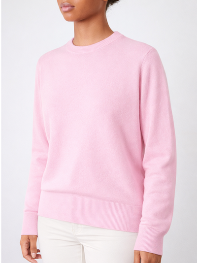 A woman wears the We Norwegians Blefjell Crewneck Women - Pure Cashmere in light pink with off-white pants, standing against a plain light background. Only her upper body is visible.