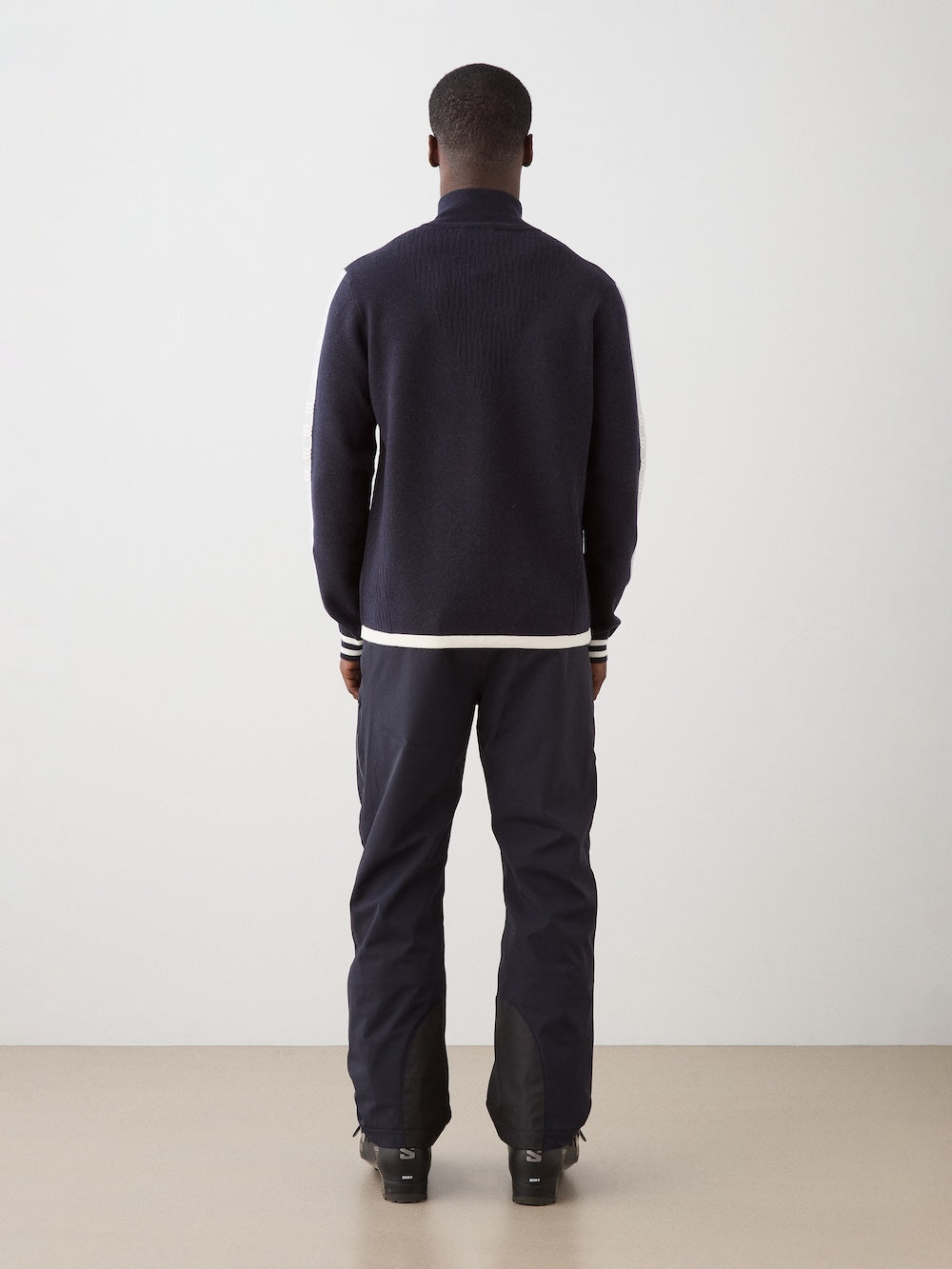 We Norwegians | FW25 | Mens Rocky Full ZipUp_Navy blue | Model wearing this fine knitted sweater with a 2-way front zipper opening, designed in a retro style with contrasting color blocks on the chest and sleeves - paired with black ski pants | Shot against an off-white background | Back