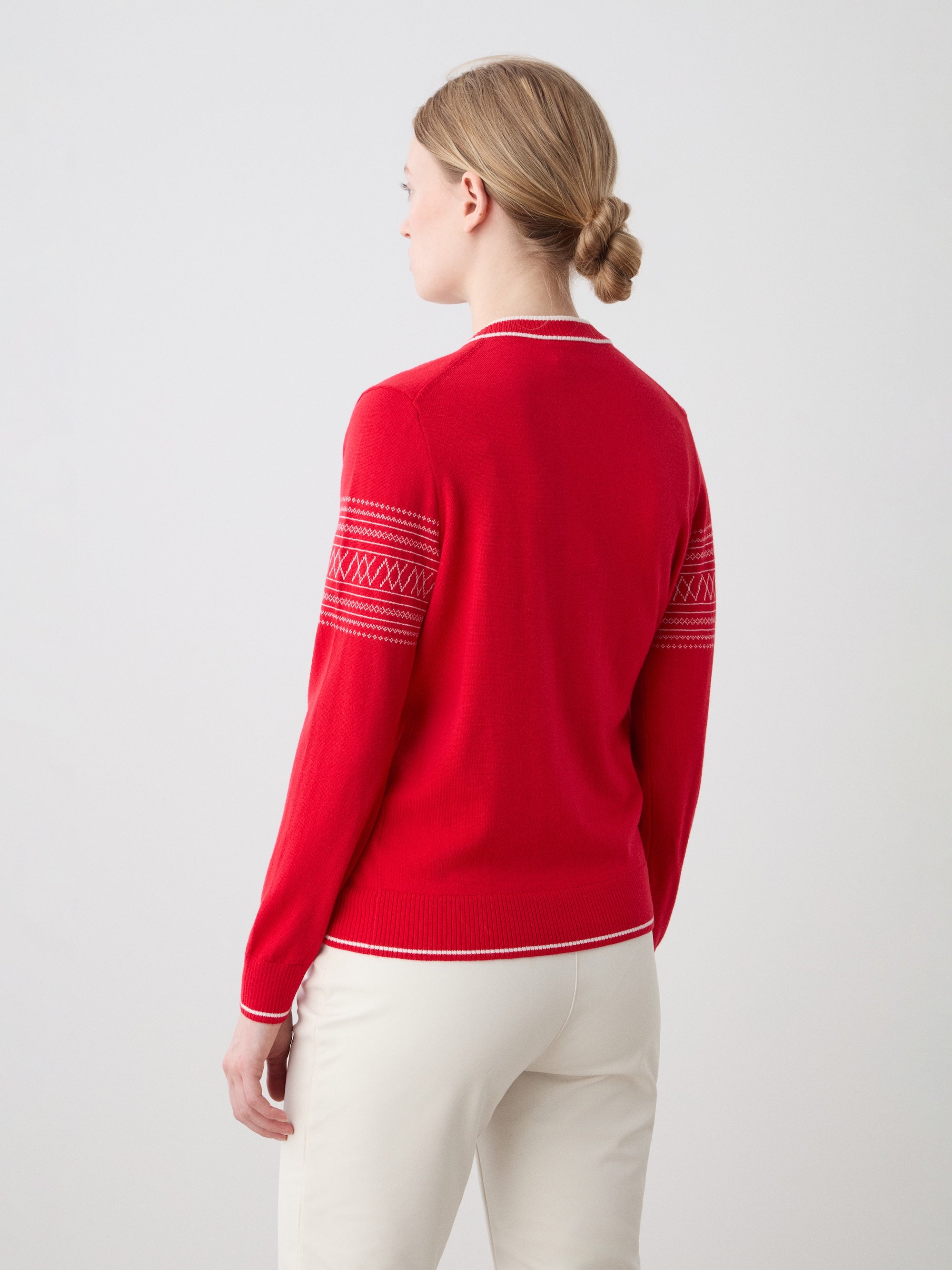 We Norwegians | FW25 | Womens Signature V-neck Sweater_Red | Model wearing this fine knitted sweater with white edges on the neckline, sleeves and hemline, with the signature setesdal pattern on the sleeves - paired with the off-white Tyin bootleg ski pants | Shot against an off-white background | Back