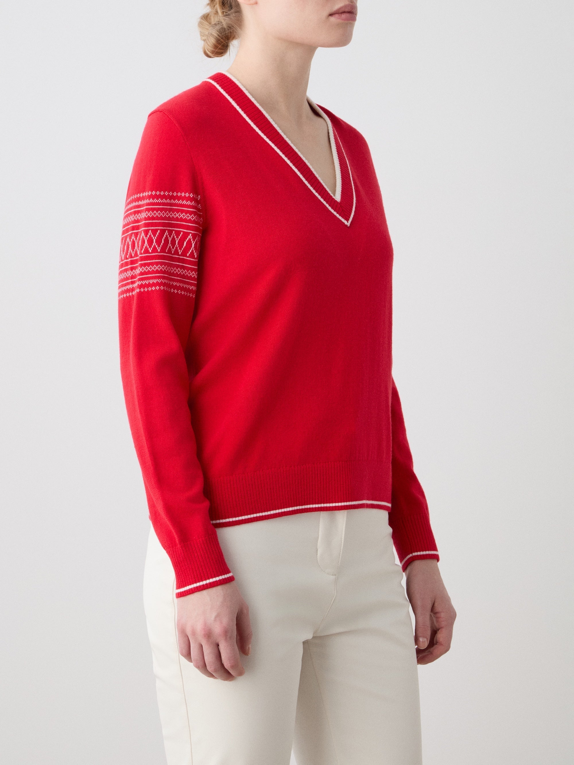 We Norwegians | FW25 | Womens Signature V-neck Sweater_Red | Model wearing this fine knitted sweater with white edges on the neckline, sleeves and hemline, with the signature setesdal pattern on the sleeves - paired with the off-white Tyin bootleg ski pants | Shot against an off-white background | Close-up