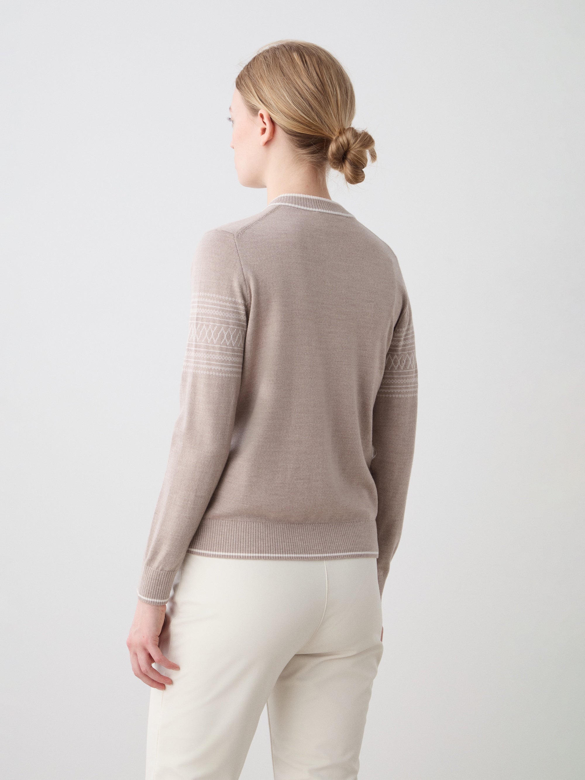 We Norwegians | FW25 | Womens Signature V-neck Sweater_Sand | Model wearing this fine knitted sweater with white edges on the neckline, sleeves and hemline, with the signature setesdal pattern on the sleeves - paired with the off-white Tyin bootleg ski pants | Shot against an off-white background | Back