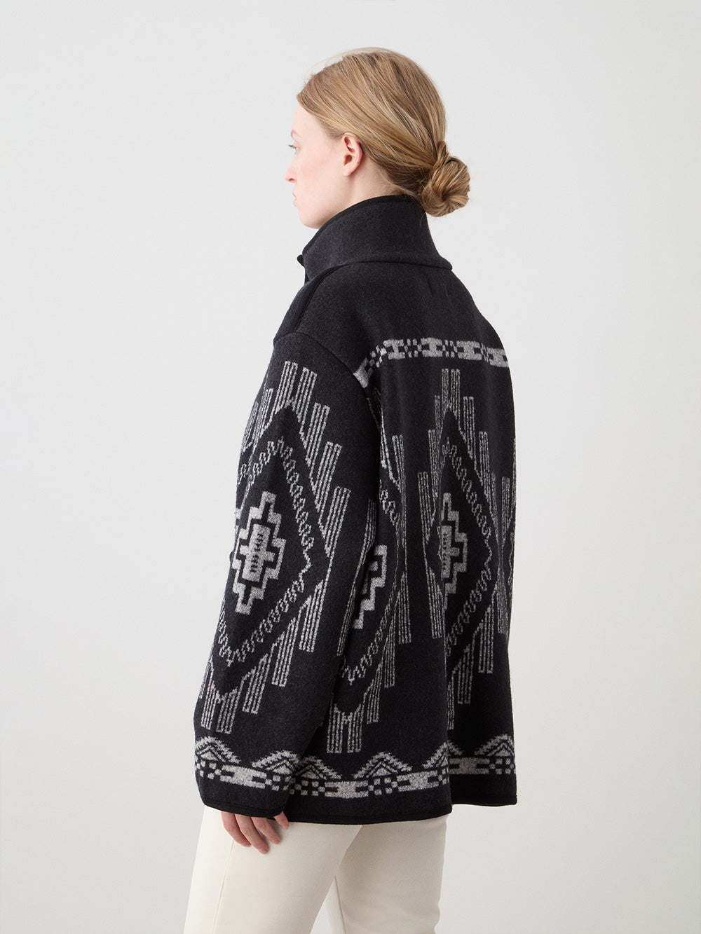 We Norwegians_FW25_Womens | Model is wearing the Kautokeino jacket in black with off white Tyin bootleg ski pants | The jacket has a bold jacquard pattern inspired by Native and Indigenous American art | Back view against a white background