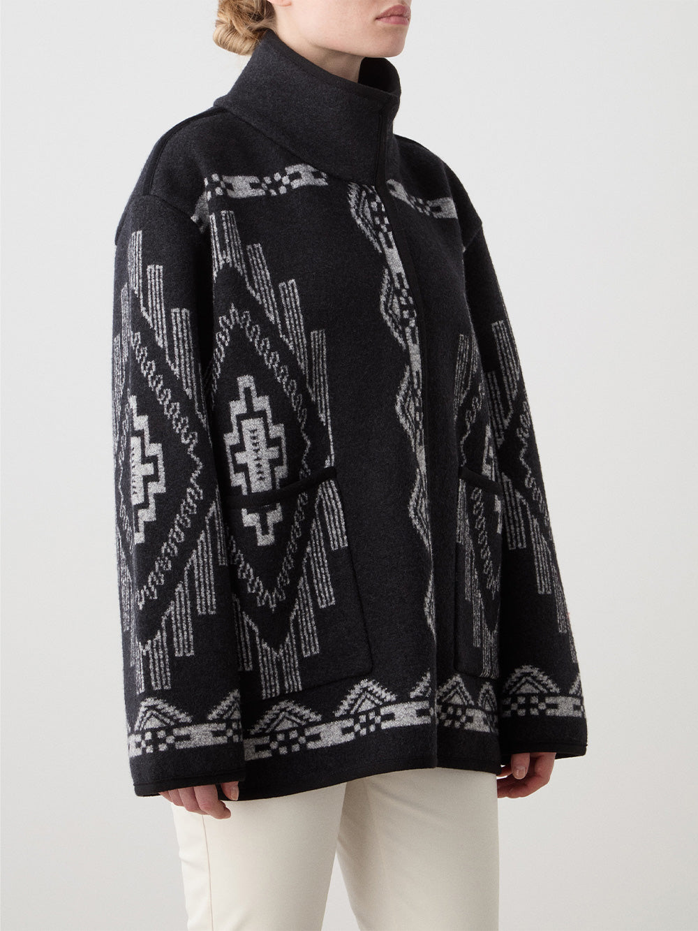 We Norwegians_FW25_Womens | Model is wearing the Kautokeino jacket in black with off white Tyin bootleg ski pants | The jacket has a bold jacquard pattern inspired by Native and Indigenous American art | Photograph focussing on the pattern details against a white background