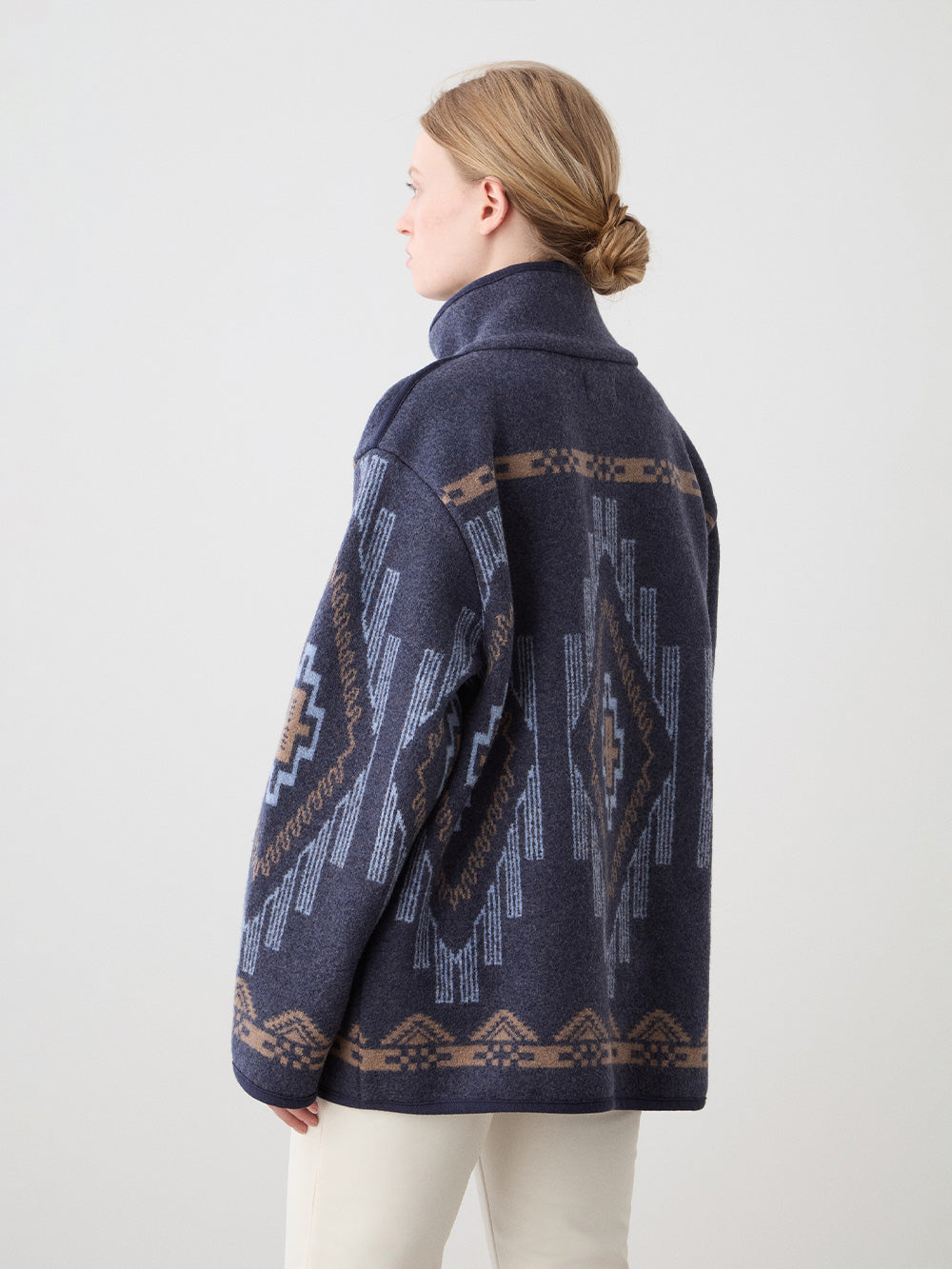 We Norwegians_FW25_Womens | Model is wearing the Kautokeino jacket in navy blue with off white Tyin bootleg ski pants | The jacket has a bold jacquard pattern inspired by Native and Indigenous American art | Back view against a white background