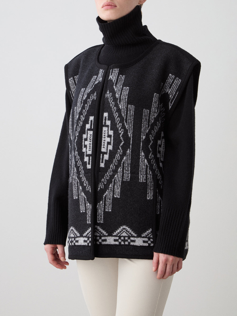 We Norwegians_FW25_Womens | Model is wearing the Kautokeino vest | Black in color with a jacquard pattern inspired by Native and Indigenous American Art | Vest has a matching belt to cinch the waist | Photograph shows the details of the garment on a white background