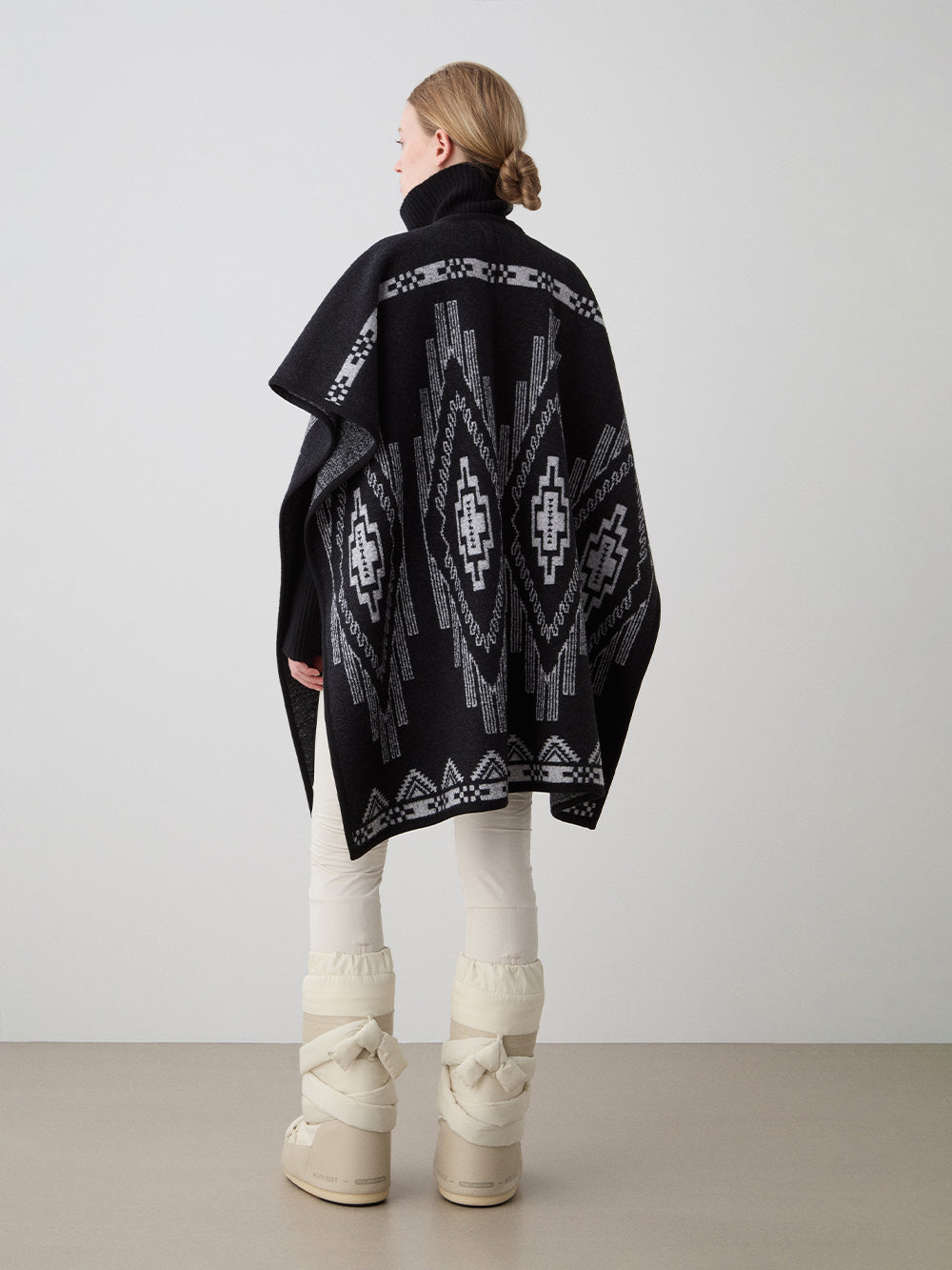 We Norwegians_FW25_Womens | Model is wearing the Kautokeino poncho | Black in color with a jacquard pattern inspired by Native and Indigenous American art | Made with boiled merino wool | Back view