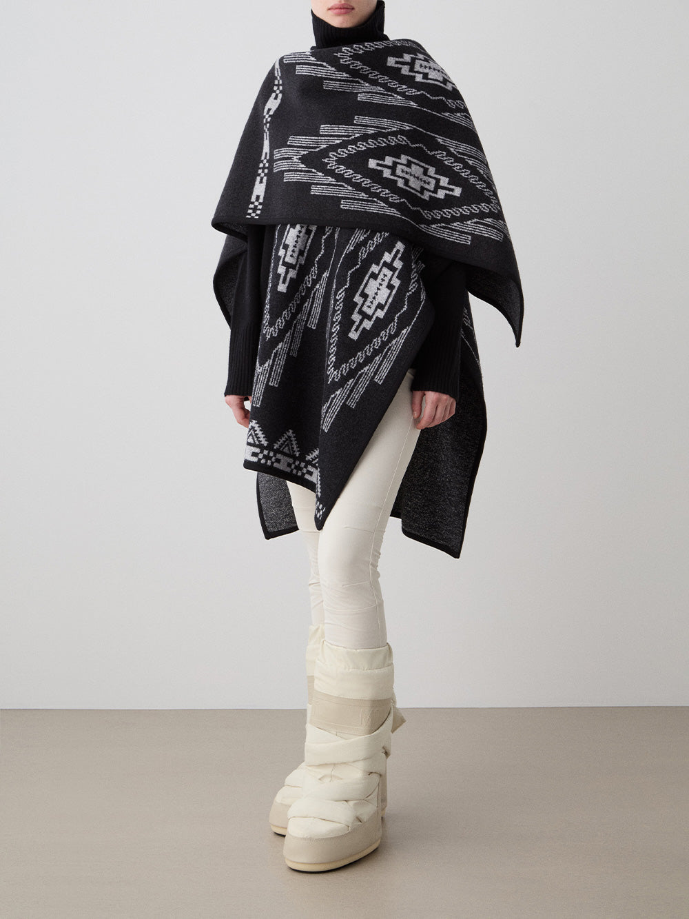 We Norwegians_FW25_Womens | Model is wearing the Kautokeino poncho | Black in color with a jacquard pattern inspired by Native and Indigenous American art | Made with boiled merino wool | Photograph showing the fall and drape features of the garment