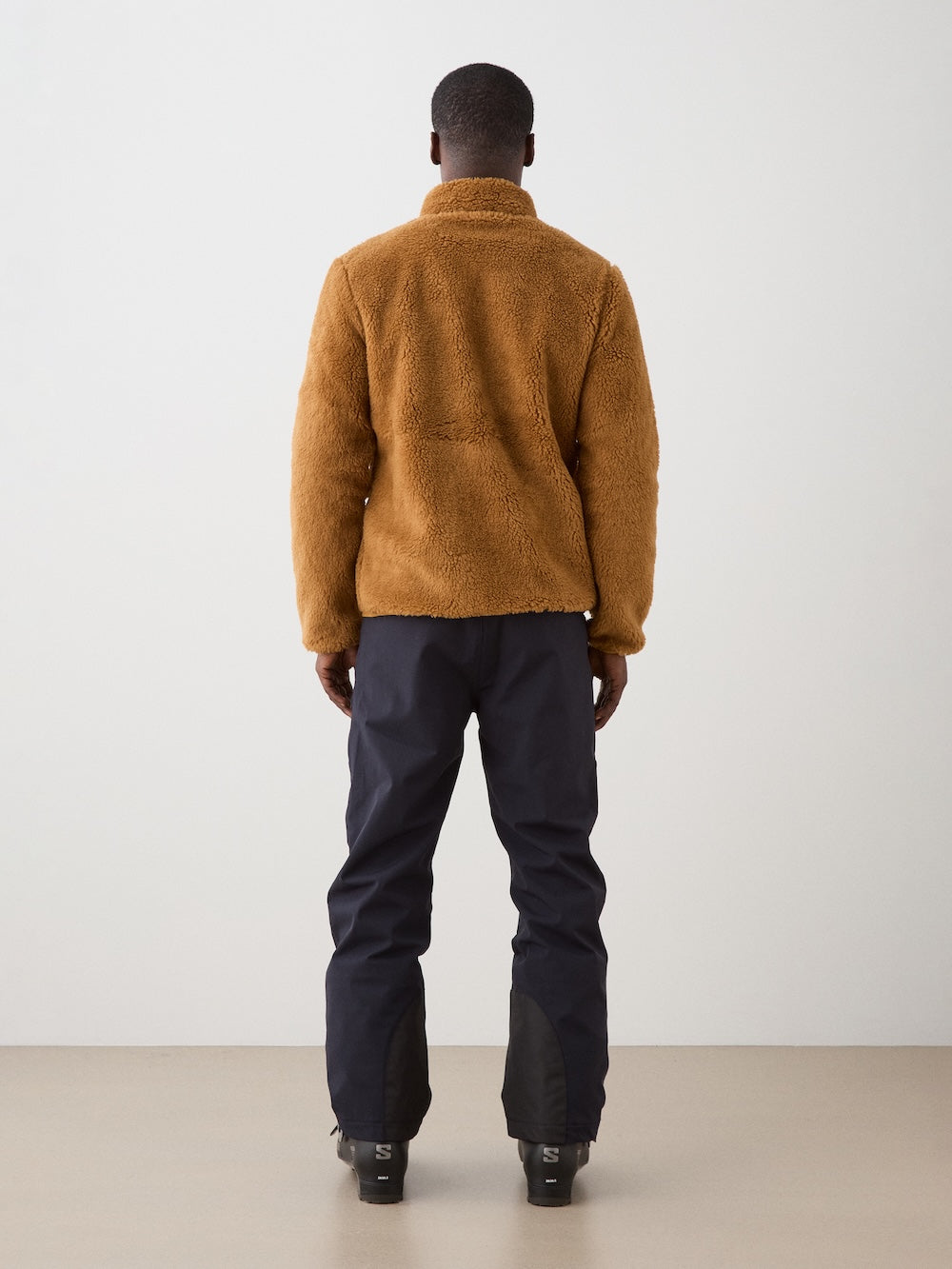 We Norwegians | FW25 | Mens Kebnekaise Jacket_Cinnamon | Model wearing this fleece jacket with front zipper opening, zipped chest pocket and side pockets - paired with black ski pants | Shot against an off-white background | Back