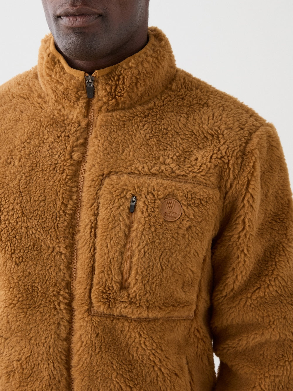 We Norwegians | FW25 | Mens Kebnekaise Jacket_Cinnamon | Model wearing this fleece jacket with front zipper opening, zipped chest pocket and side pockets - paired with black ski pants | Shot against an off-white background | Close-up