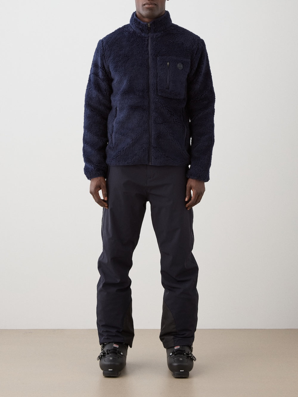 We Norwegians | FW25 | Mens Kebnekaise Jacket_Navy blue | Model wearing this fleece jacket with front zipper opening, zipped chest pocket and side pockets - paired with black ski pants | Shot against an off-white background | Front