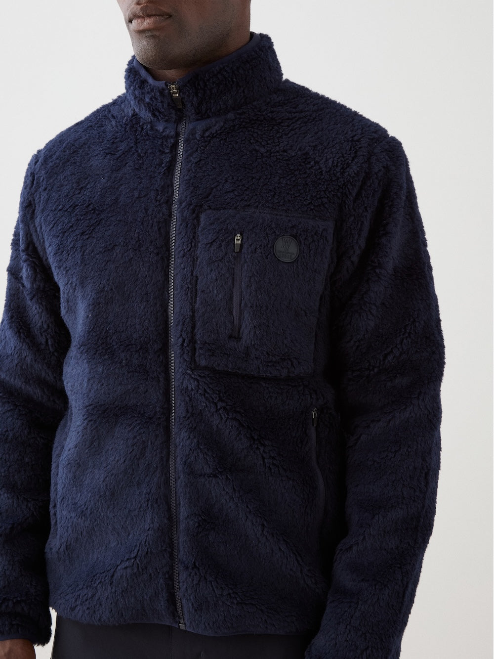We Norwegians | FW25 | Mens Kebnekaise Jacket_Navy blue | Model wearing this fleece jacket with front zipper opening, zipped chest pocket and side pockets - paired with black ski pants | Shot against an off-white background | Close-up