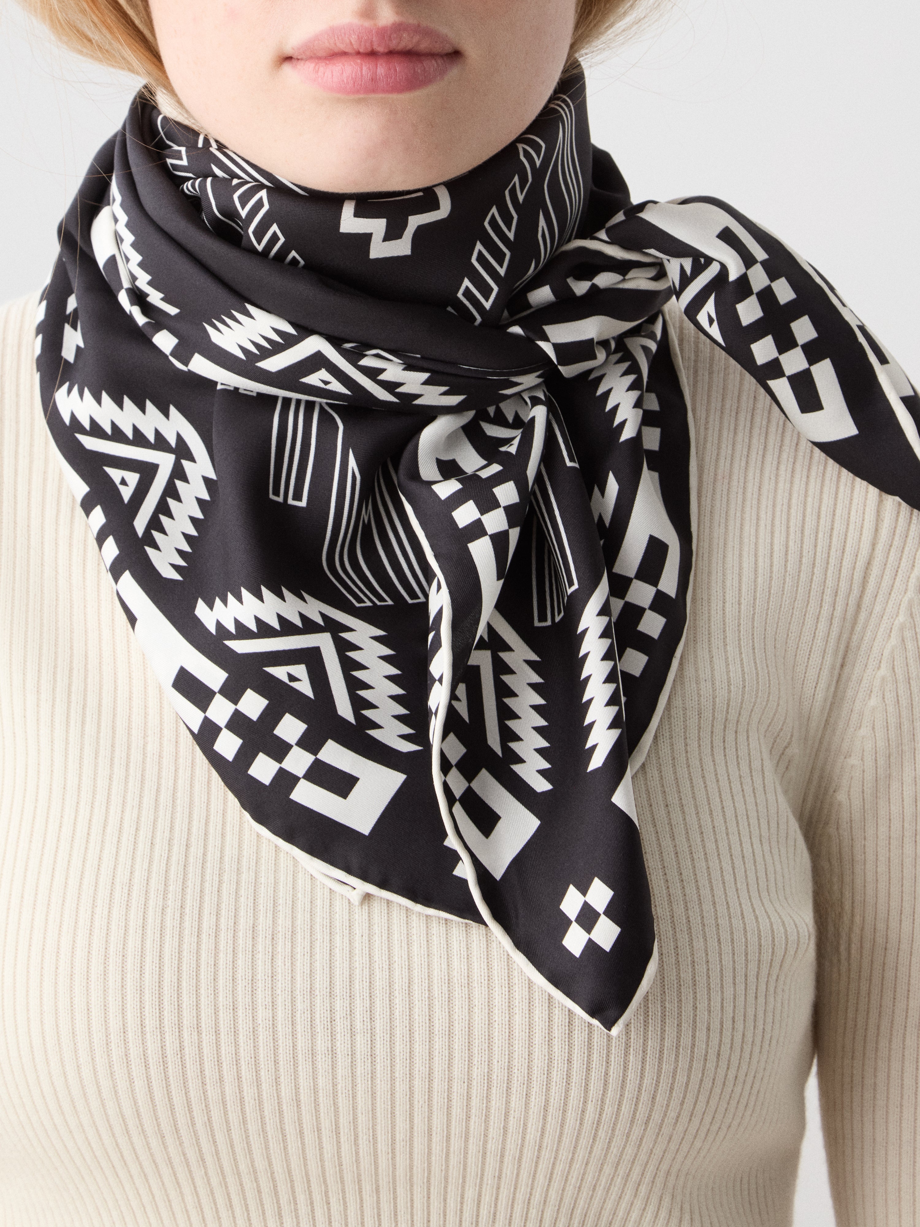 We Norwegians | FW25 | Pioneer Silk Scarf_Black | Female model wearing the scarf with printed motifs over a light top | Shot against an off-white background
