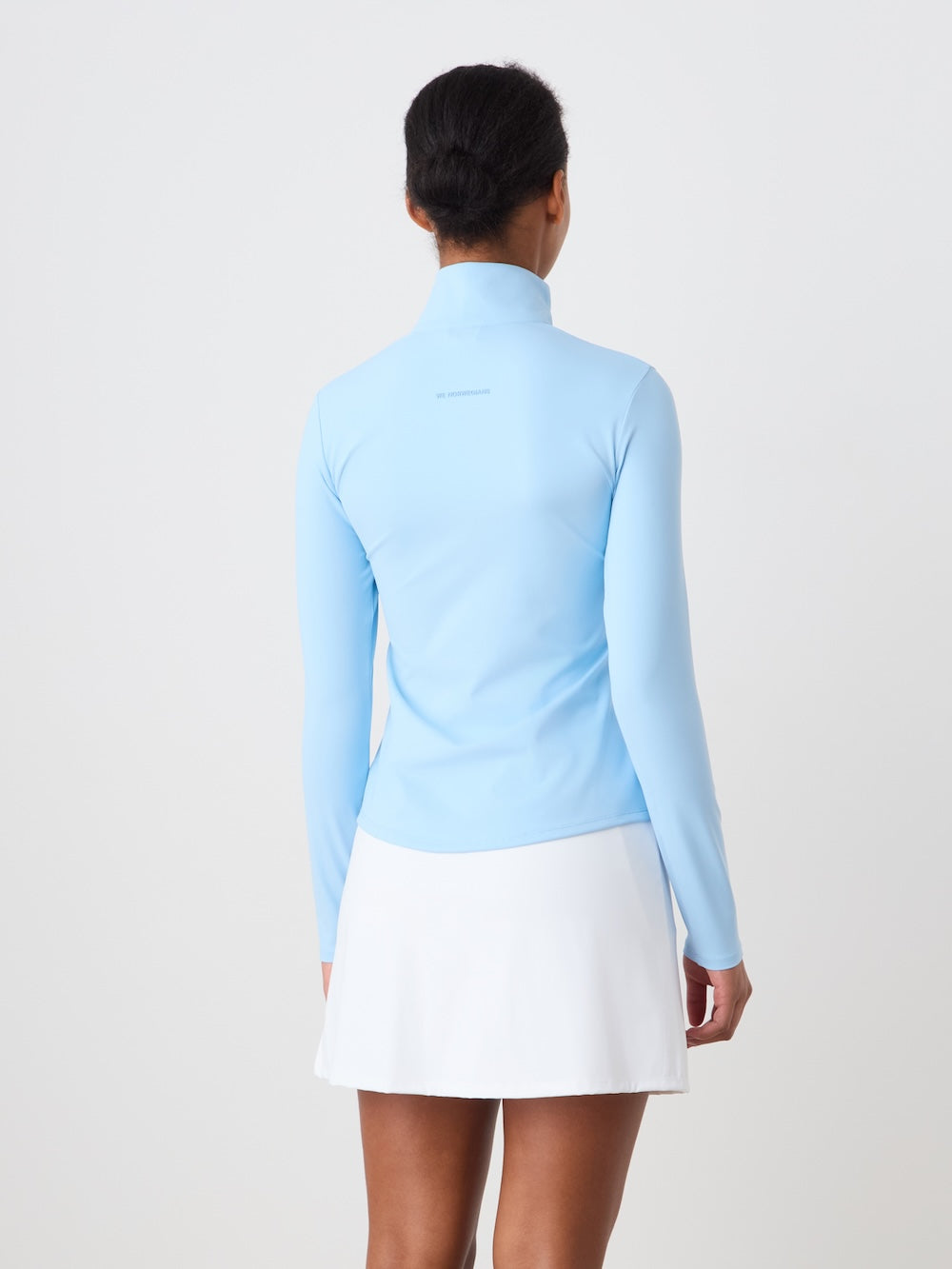 Person wearing a light blue long-sleeve top and white skirt on a plain background