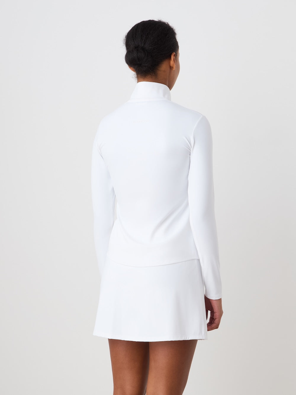 Person wearing the white Honor zipped long sleeve with a white skirt against a plain background_Back