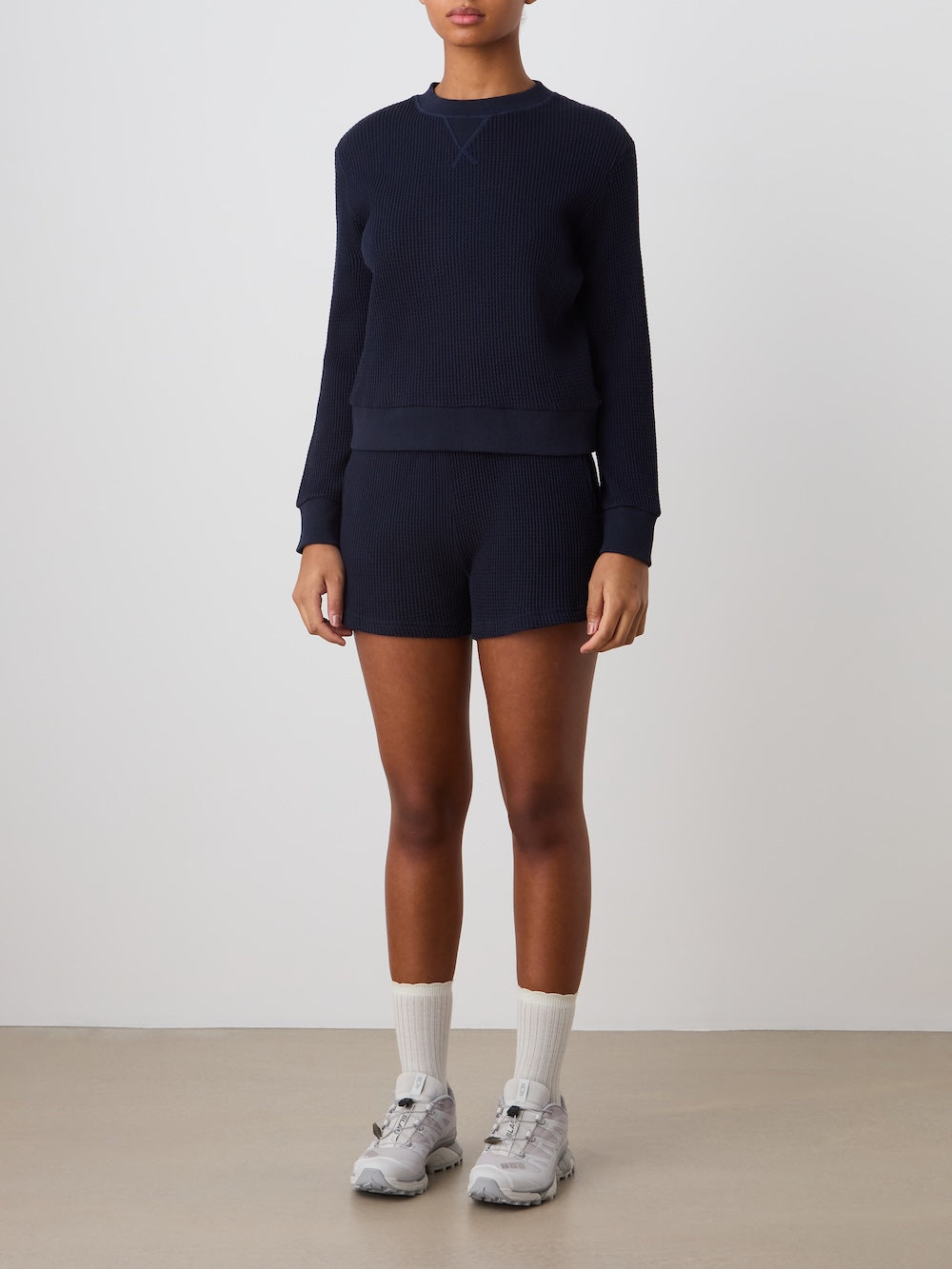 Person wearing a navy blue crewneck and shorts set with white socks and sneakers on a plain background