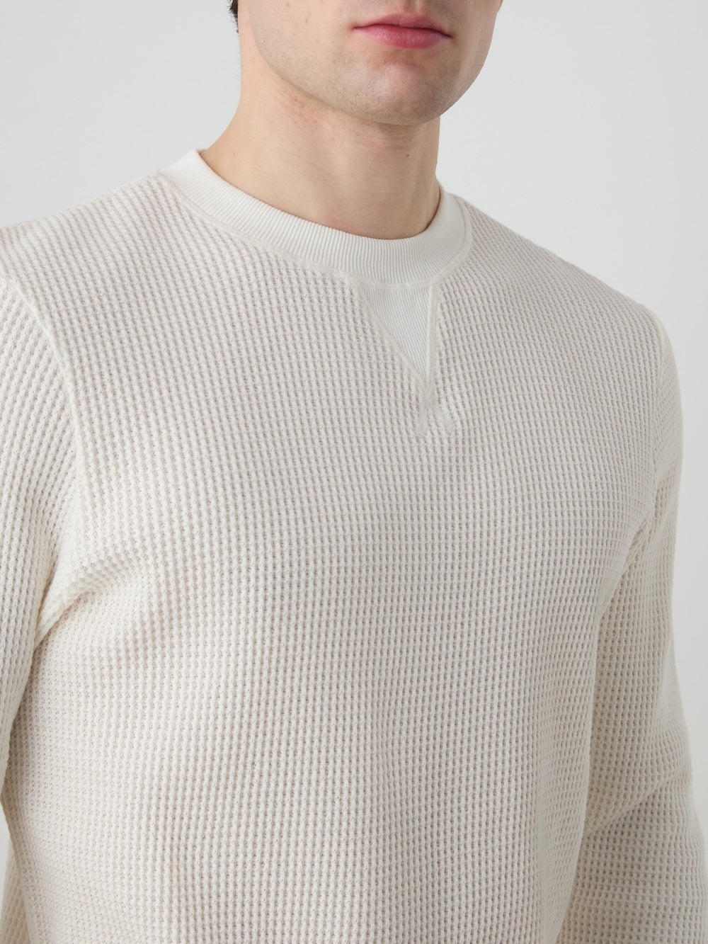 Close-up of a person wearing an off white waffle crewneck against a light background