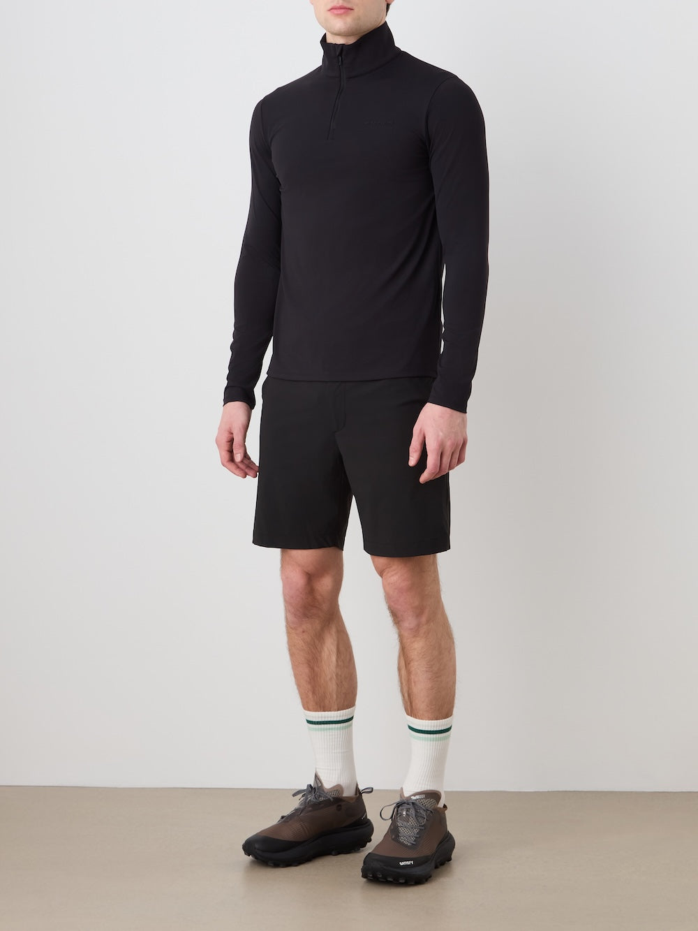 Person wearing a black turtleneck, black shorts, and brown shoes on a plain background
