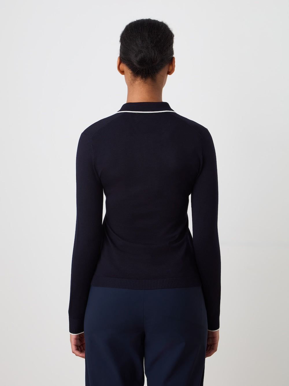 Person wearing a navy blue polo shirt with a white details on a light background