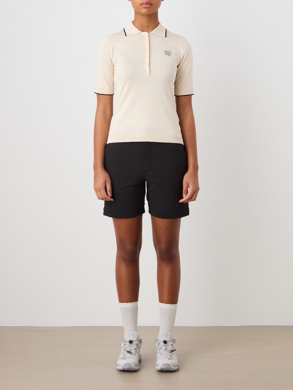 Person wearing a beige polo shirt and black shorts on a plain background