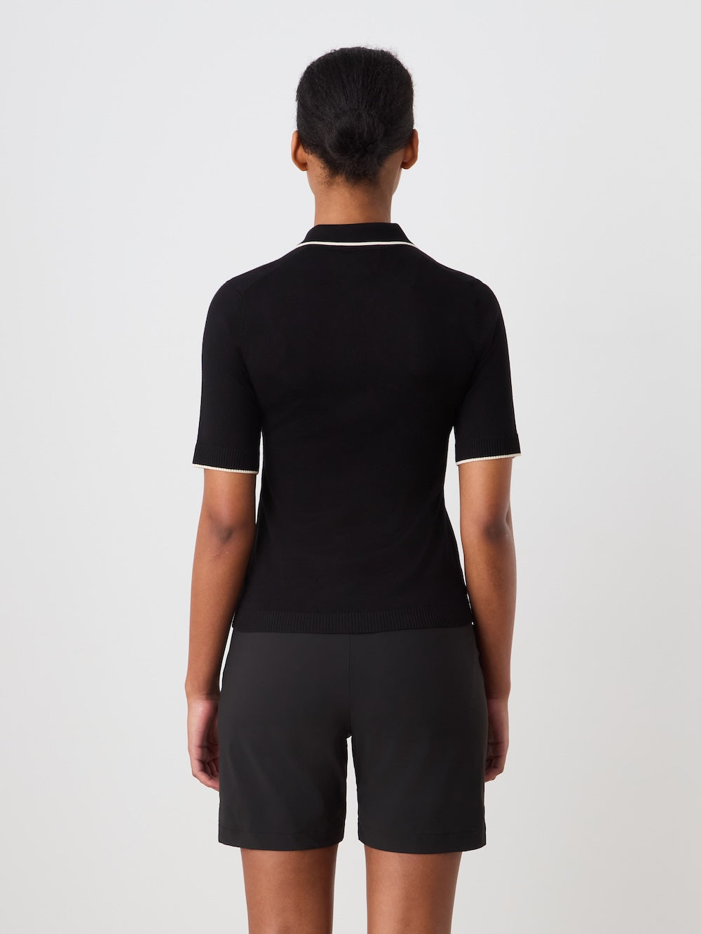 Person wearing a black polo shirt with white details on a plain background