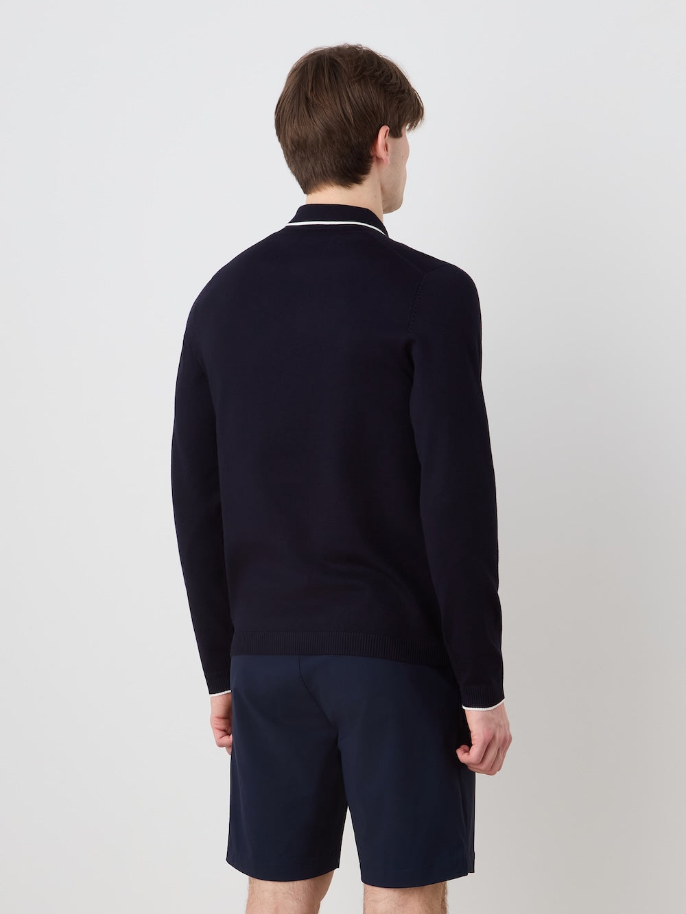 Person wearing a navy blue long sleeved polo and shorts on a light background