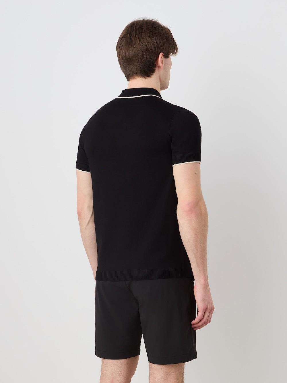Person wearing a black polo shirt and shorts on an off white background
