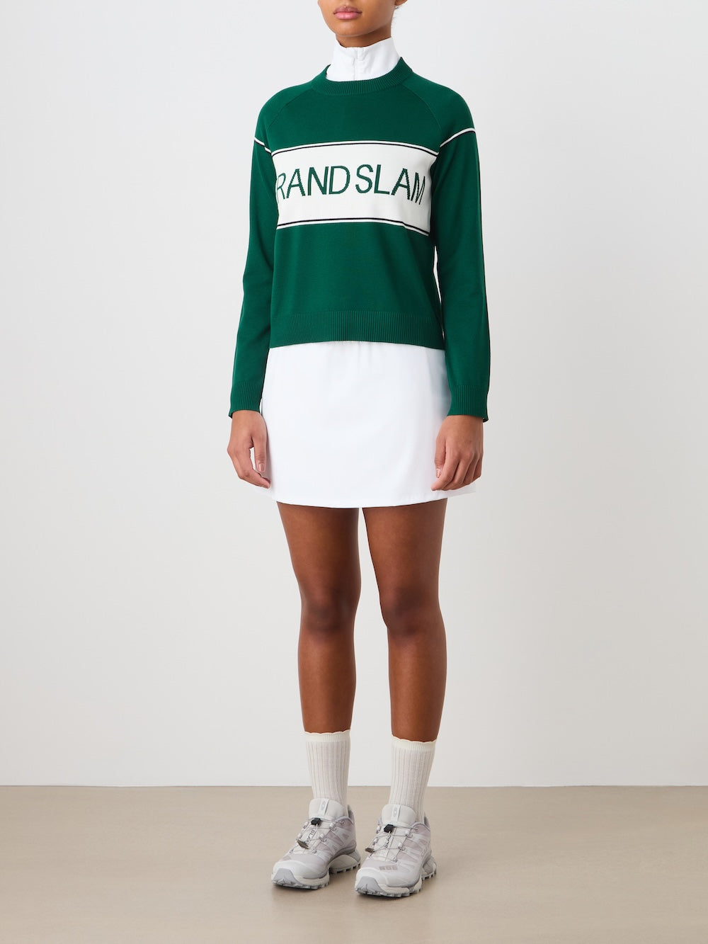 Person wearing the green "Grand Slam" sweater with a white skirt, socks and sneakers against a plain background