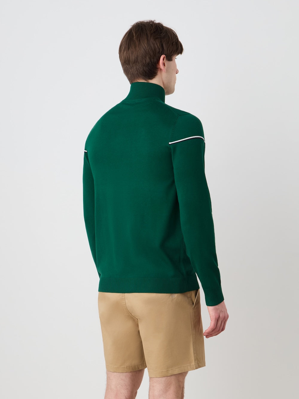 Person wearing a Green sweater with a "Grand Slam" artwork in the front with beige shorts against a light background