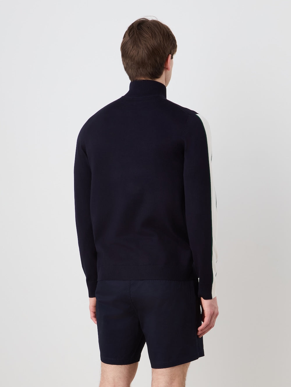 Person wearing a navy blue half-zip sweater with a "Grand Slam" artwork in the front and shorts on a light background