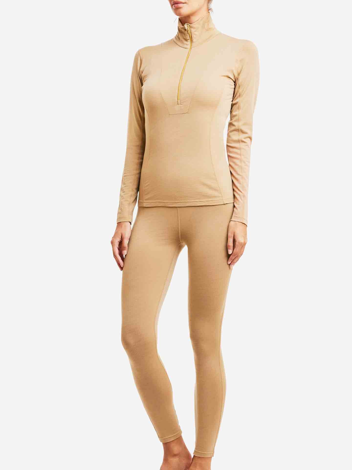 A person is wearing the Sno Merino Zip Up Women set by We Norwegians, featuring a matching tan-colored long-sleeve top and leggings. The high-neck top, with its half-zip closure, boasts a fitted shape made from super fine merino wool. Perfect for active wear or lounging, this Scandinavian luxury base-layer ensures both comfort and style against the white background.