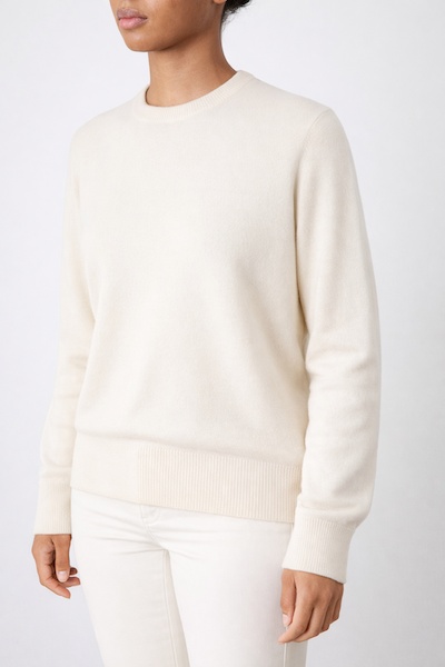 A person wears the We Norwegians Blefjell Crewneck Women sweater in pure cashmere, paired with light pants, standing against a plain light background. Their face is partially out of frame.