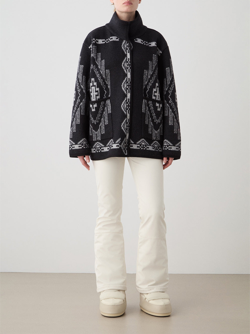 We Norwegians_FW25_Womens | Model is wearing the Kautokeino jacket in black with off white Tyin bootleg ski pants | The jacket has a bold jacquard pattern inspired by Native and Indigenous American art | Front view against a white background