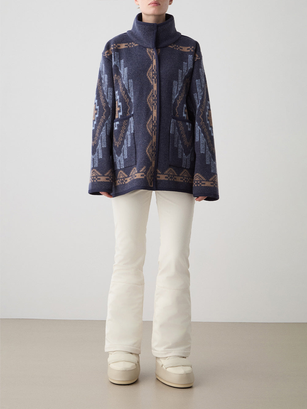 We Norwegians_FW25_Womens | Model is wearing the Kautokeino jacket in navy blue with off white Tyin bootleg ski pants | The jacket has a bold jacquard pattern inspired by Native and Indigenous American art | Front view against a white background