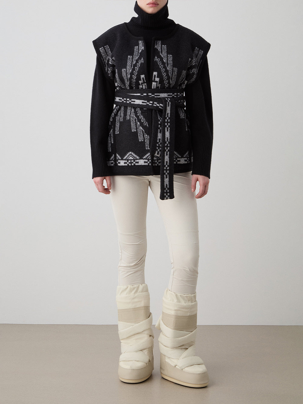We Norwegians_FW25_Womens | Model is wearing the Kautokeino vest | Black in color with a jacquard pattern inspired by Native and Indigenous American Art | Vest has a matching belt to cinch the waist | Front view on a white background