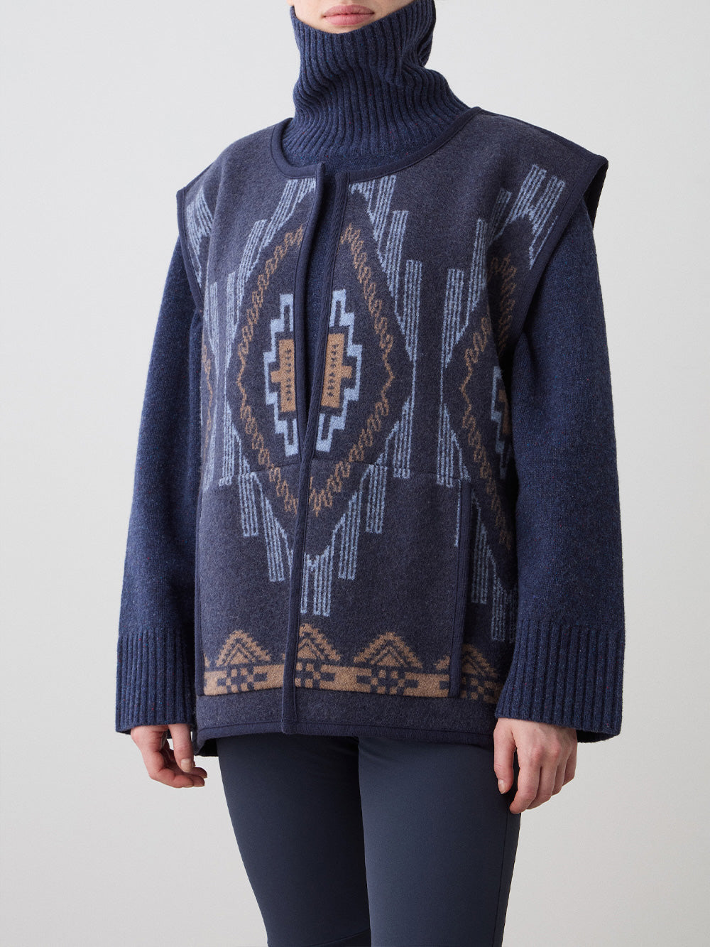 We Norwegians_FW25_Womens | Model is wearing the Kautokeino vest | Navy blue in color with a jacquard pattern inspired by Native and Indigenous American Art | Vest has a matching belt to cinch the waist | Photograph is showing the details of the garment on a white background