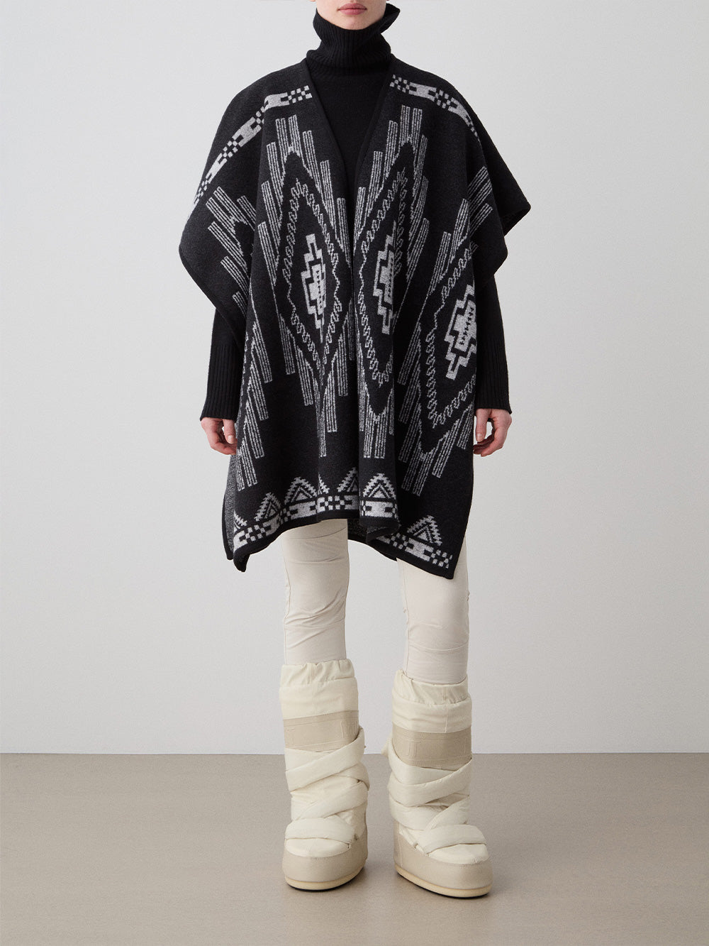 We Norwegians_FW25_Womens | Model is wearing the Kautokeino poncho | Black in color with a jacquard pattern inspired by Native and Indigenous American art | Made with boiled merino wool | Front view