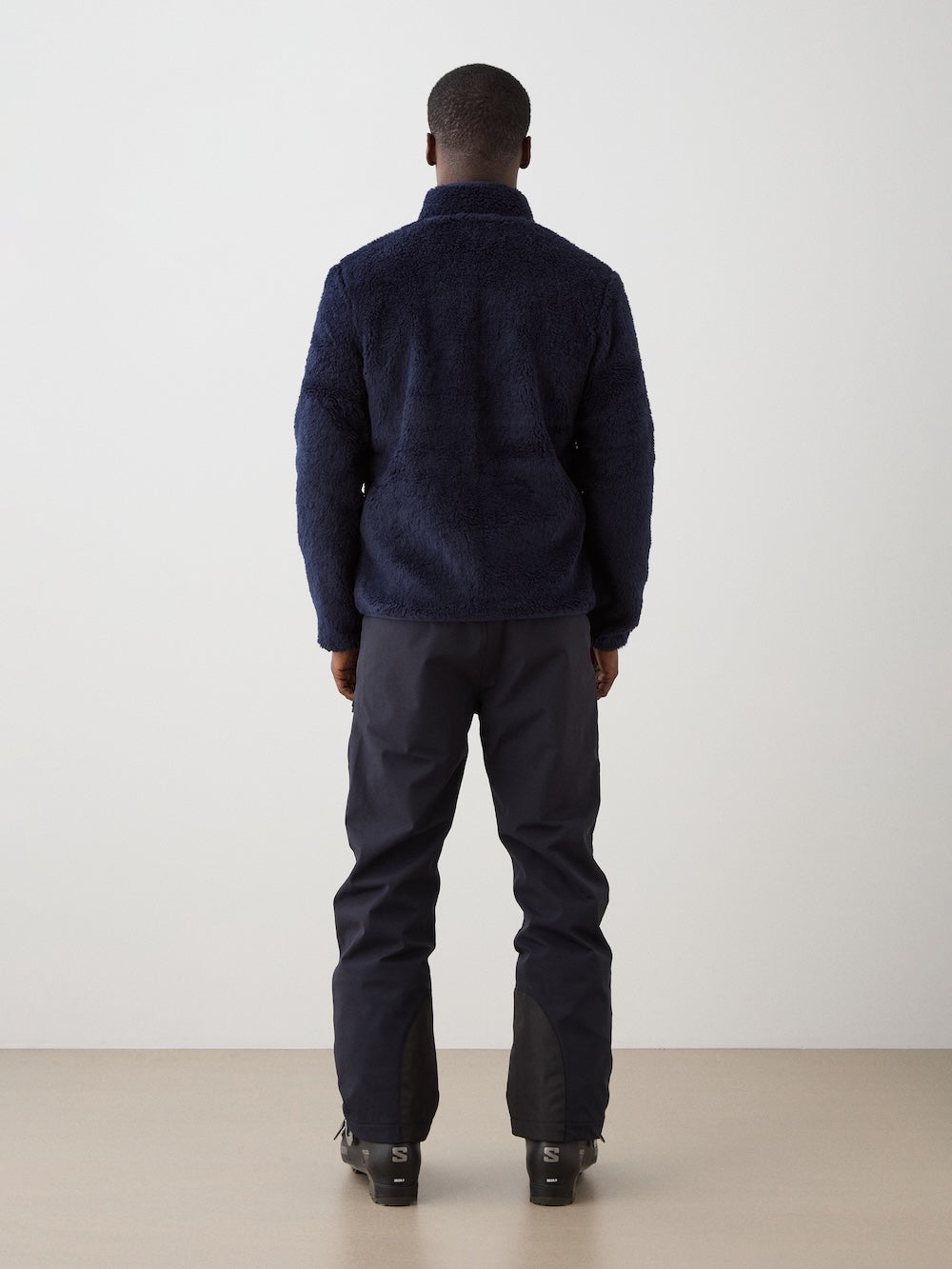 We Norwegians | FW25 | Mens Kebnekaise Jacket_Navy blue | Model wearing this fleece jacket with front zipper opening, zipped chest pocket and side pockets - paired with black ski pants | Shot against an off-white background | Back