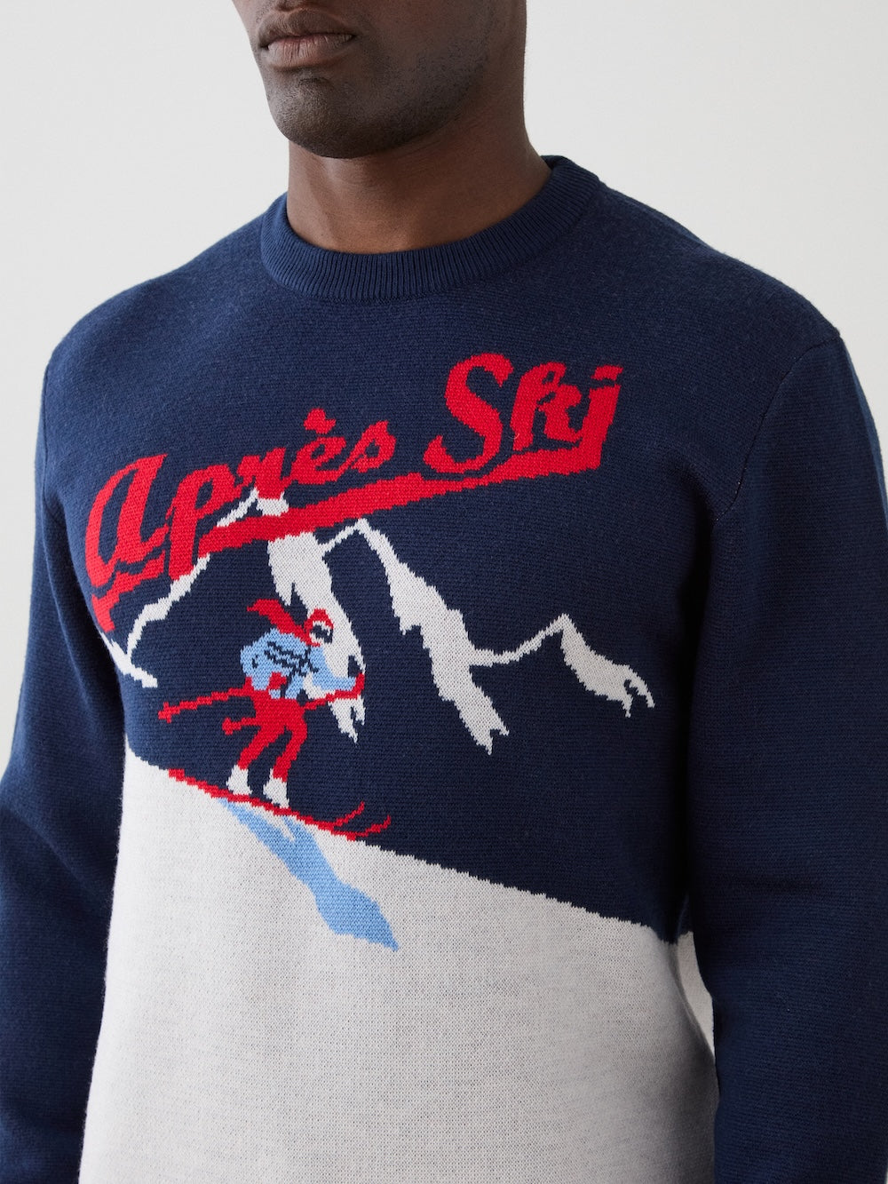 We Norwegians | FW25 | Mens Afterski Crewneck_Navy blue | Model wearing a knitted sweater with an après ski design at the front | Shot against an off-white background | Close-up view