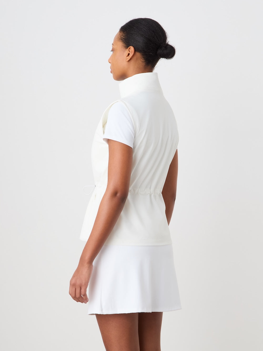 Woman wearing a white vest with a matching skirt against a plain background