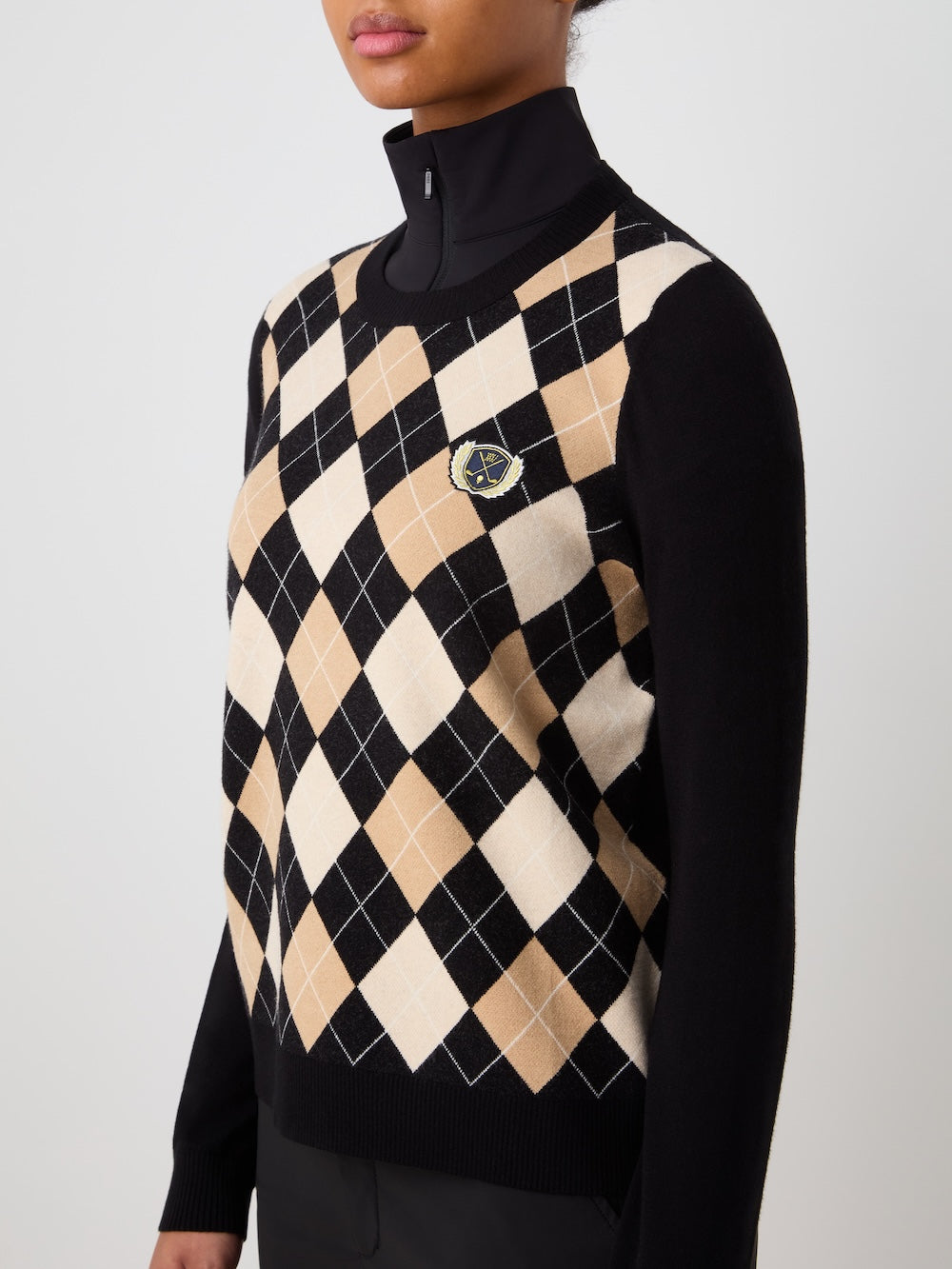 Person wearing the black Fairway sweater with argyle pattern over a black turtleneck against a light background