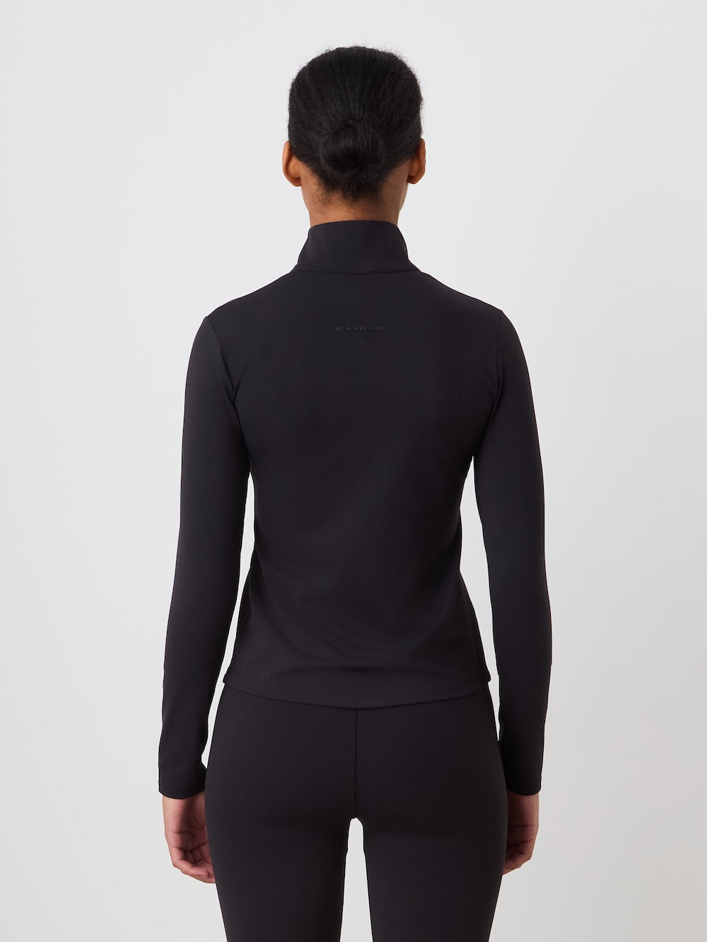 Person wearing a black long-sleeve top and pants on a light background