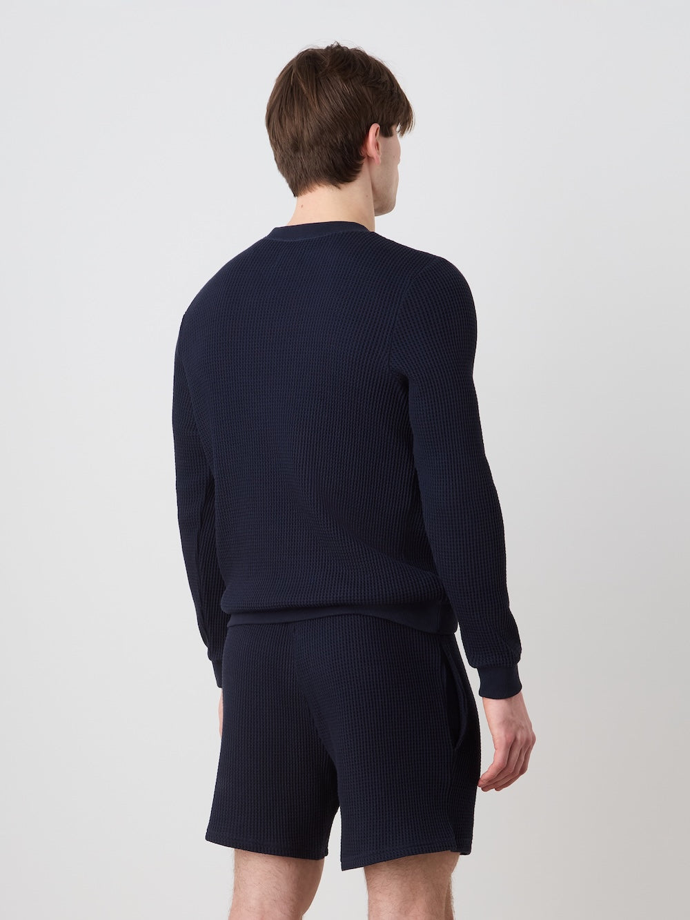 Person wearing a navy blue crewneck and shorts on a light background