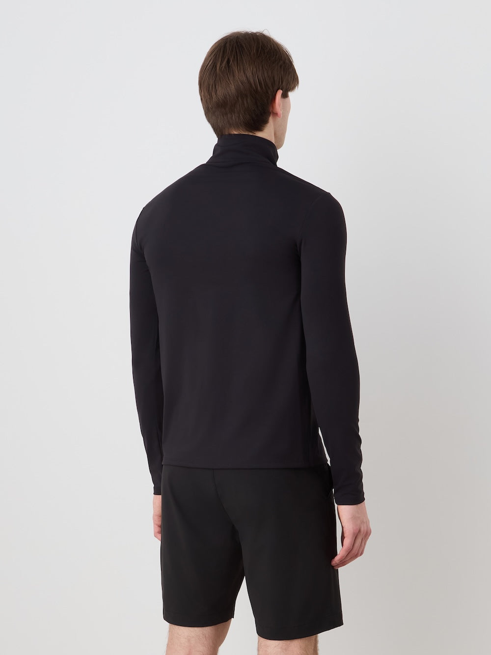 Person wearing a black long-sleeve shirt and black shorts on a light background