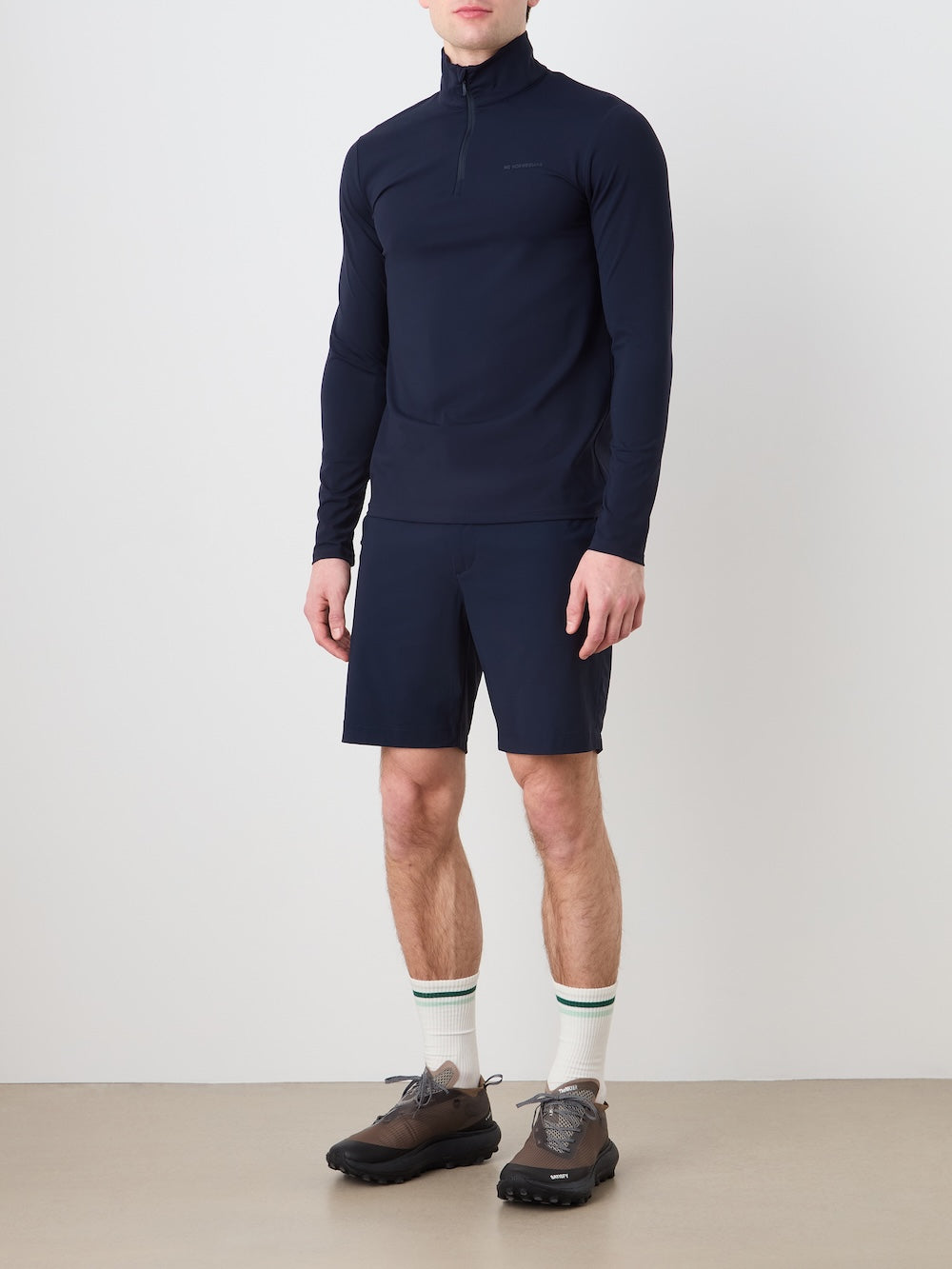 Person wearing a navy long-sleeve shirt and shorts with white socks on a plain background