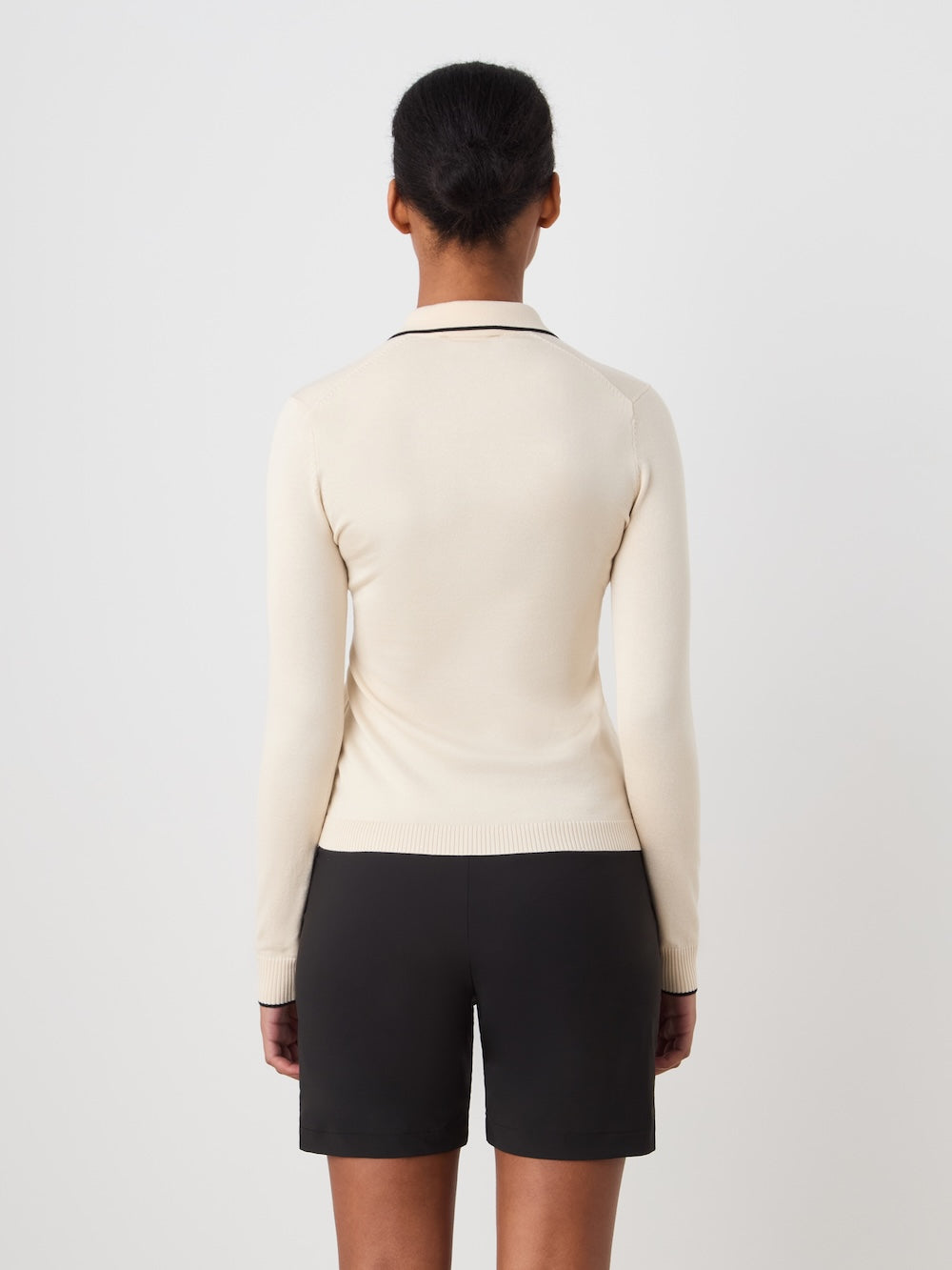 Person wearing a beige long-sleeve polo and black shorts on a plain background