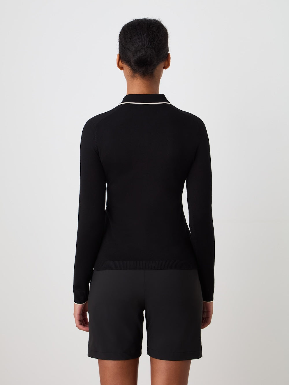 Person wearing a black long-sleeve polo and shorts on a light background