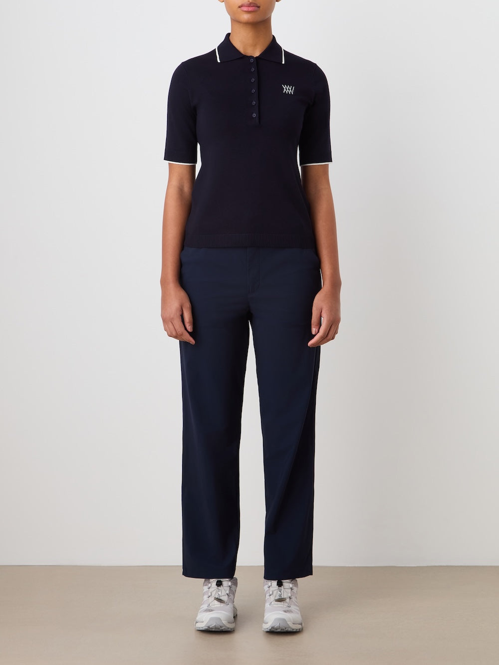 Person wearing a navy blue polo shirt and pants with a white logo on a plain background