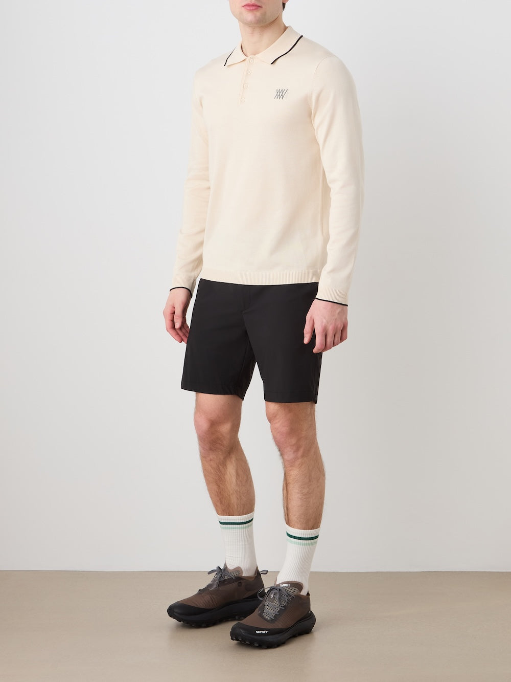 Person wearing a beige long sleeved polo, black shorts on a plain background