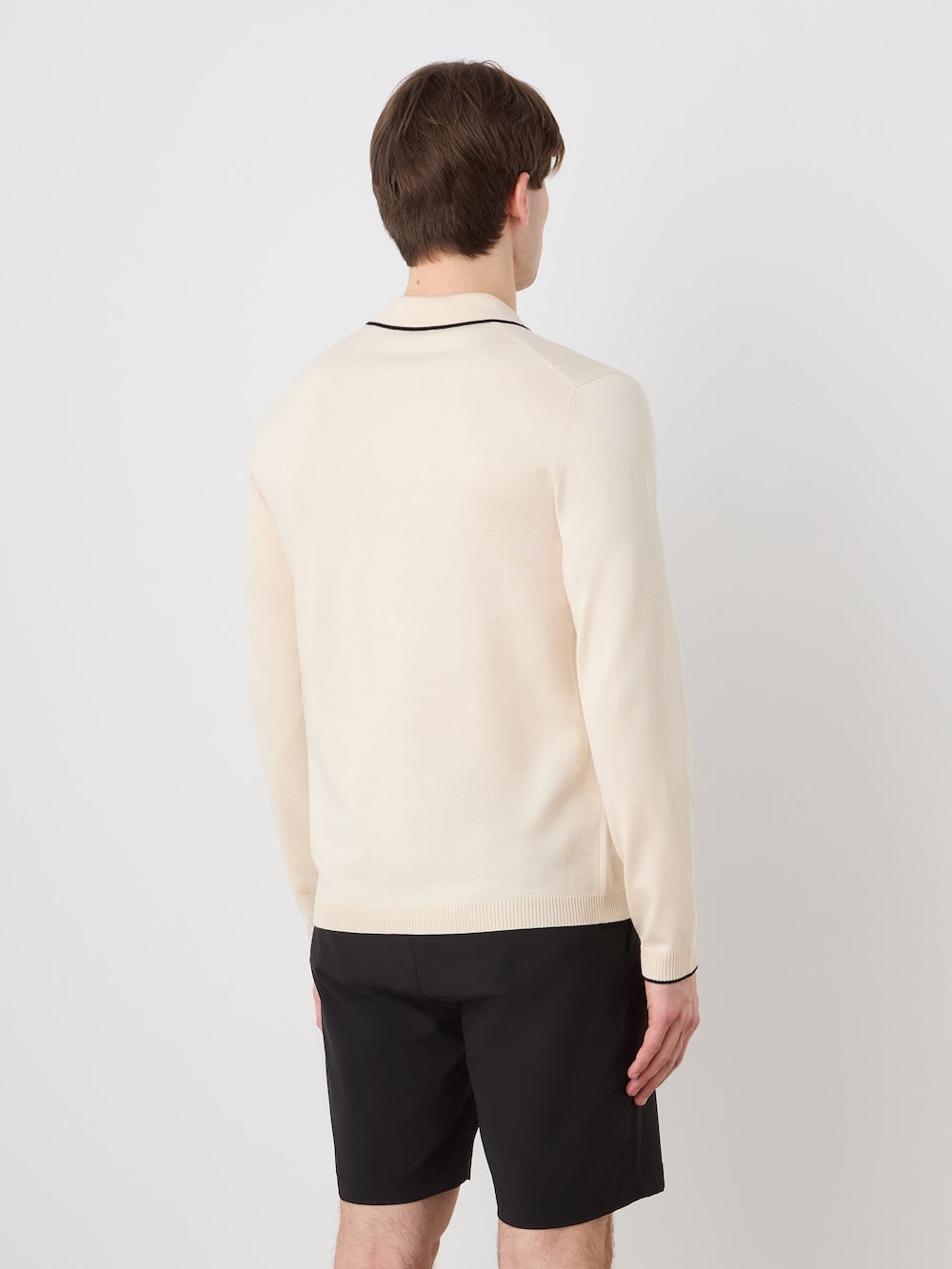 Person wearing a beige long sleeved polo with black details on a light background